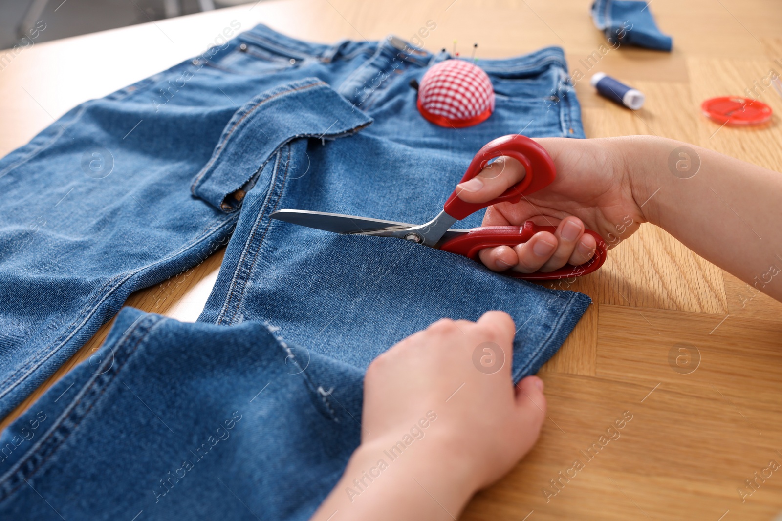 Photo of Woman cutting jeans with scissors at wooden table, closeup