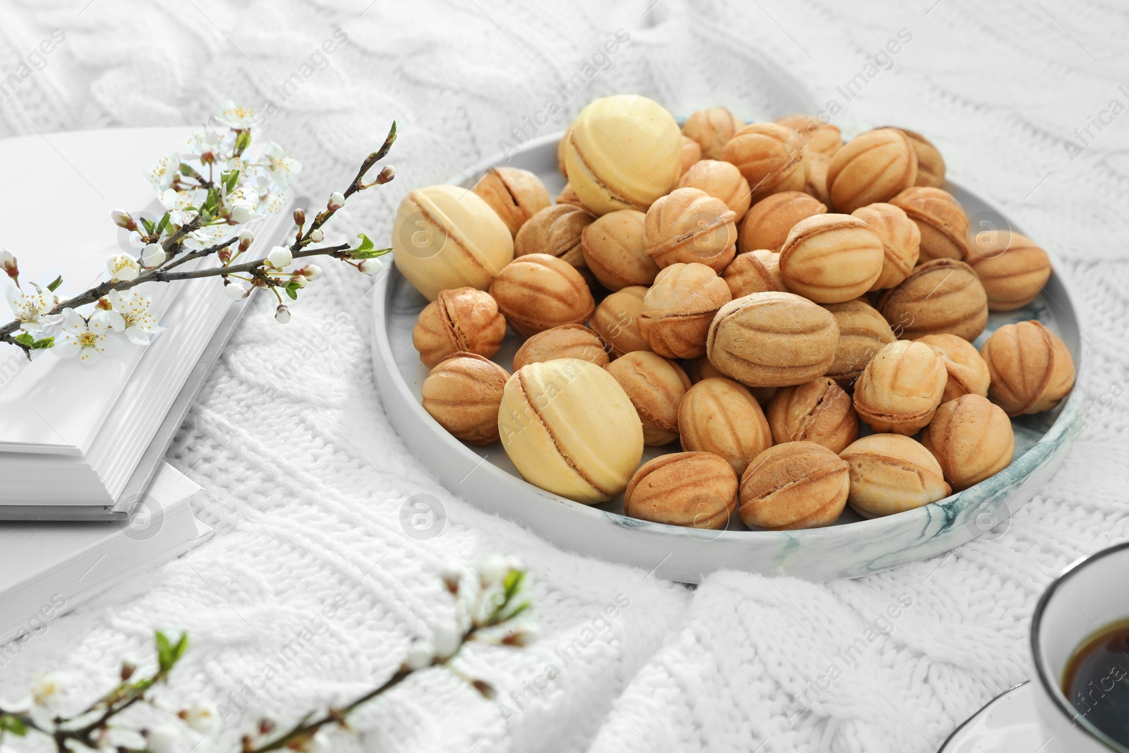 Photo of Delicious walnut shaped cookies with filling, cherry branch, notebook and cup of coffee on white knitted blanket. Homemade popular biscuits from childhood