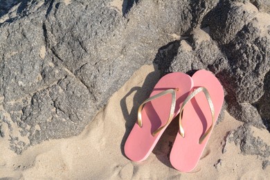 Photo of Stylish pink flip flops on sandy beach near rocks, flat lay