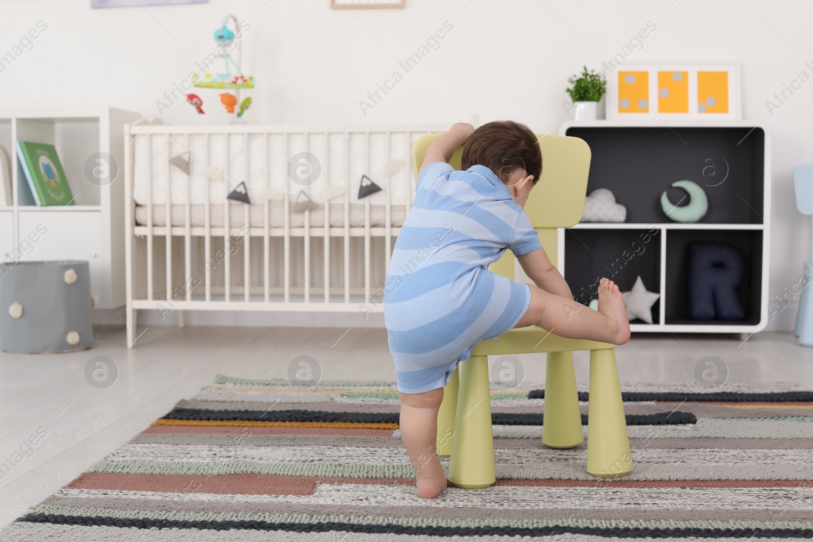 Photo of Cute baby climbing on chair at home. Learning to walk