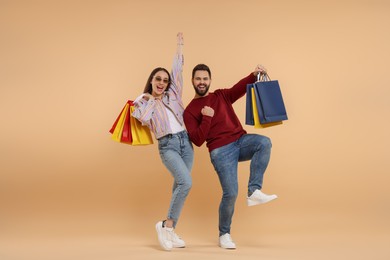 Excited couple with shopping bags having fun on beige background