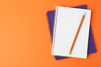 Photo of Notebooks with pencil on orange background, top view. Space for text