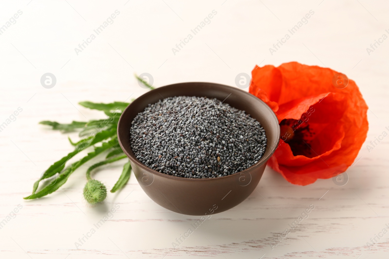 Photo of Bowl of poppy seeds and flower on white wooden table