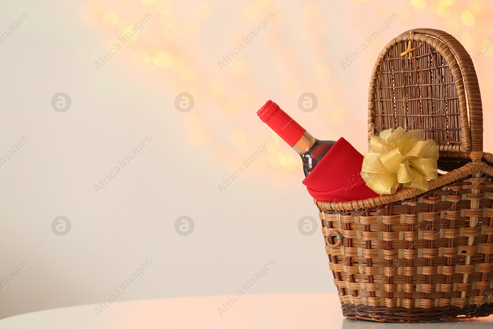 Photo of Wicker basket with bottle of wine against blurred background. Space for text