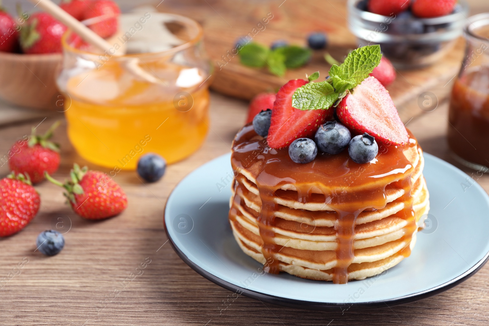 Photo of Delicious pancakes with fresh berries and syrup on wooden table