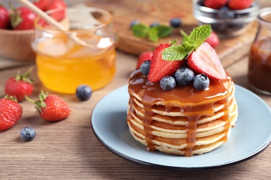 Delicious pancakes with fresh berries and syrup on wooden table