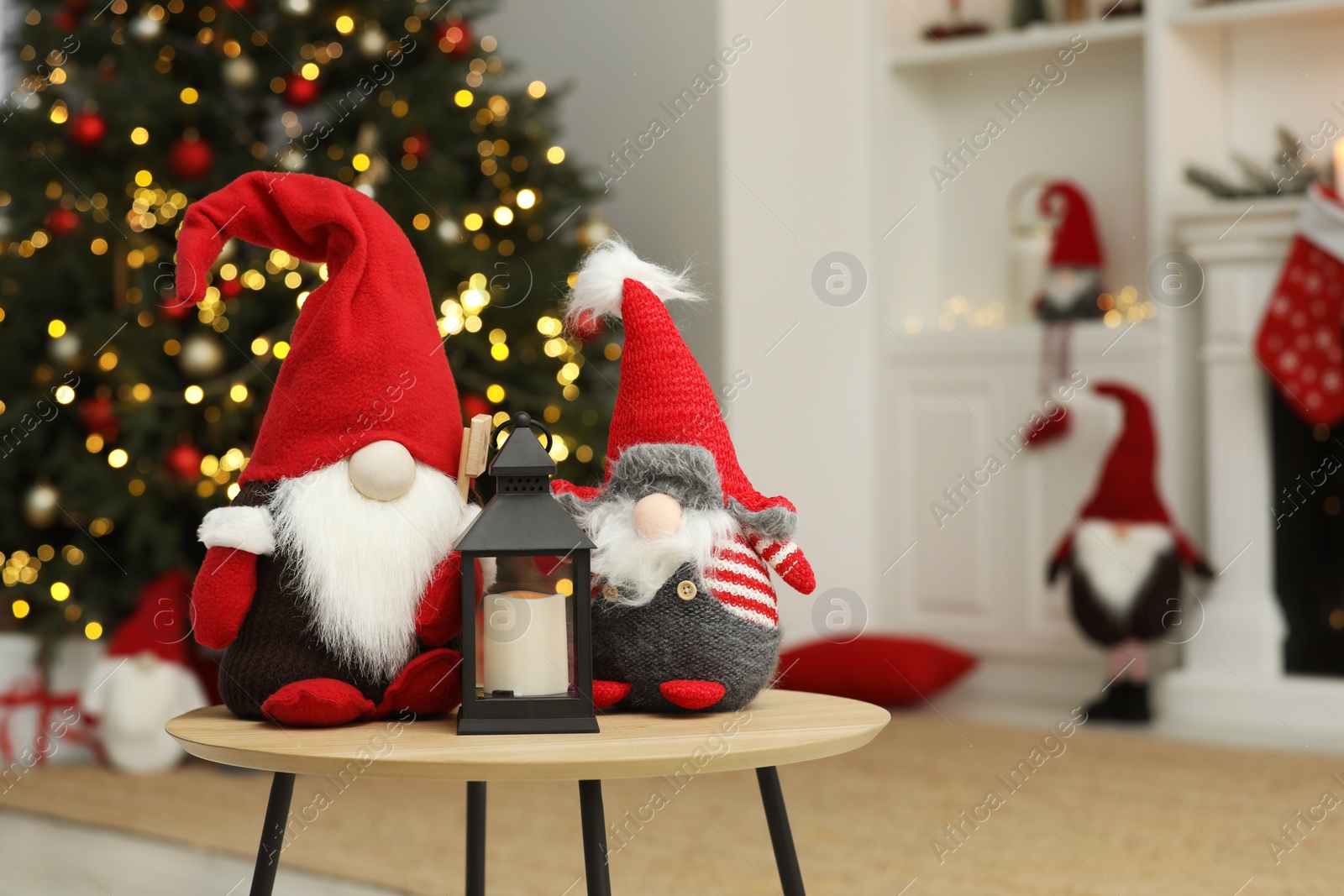 Photo of Funny Christmas gnomes and candle holder on coffee table in room with festive decoration