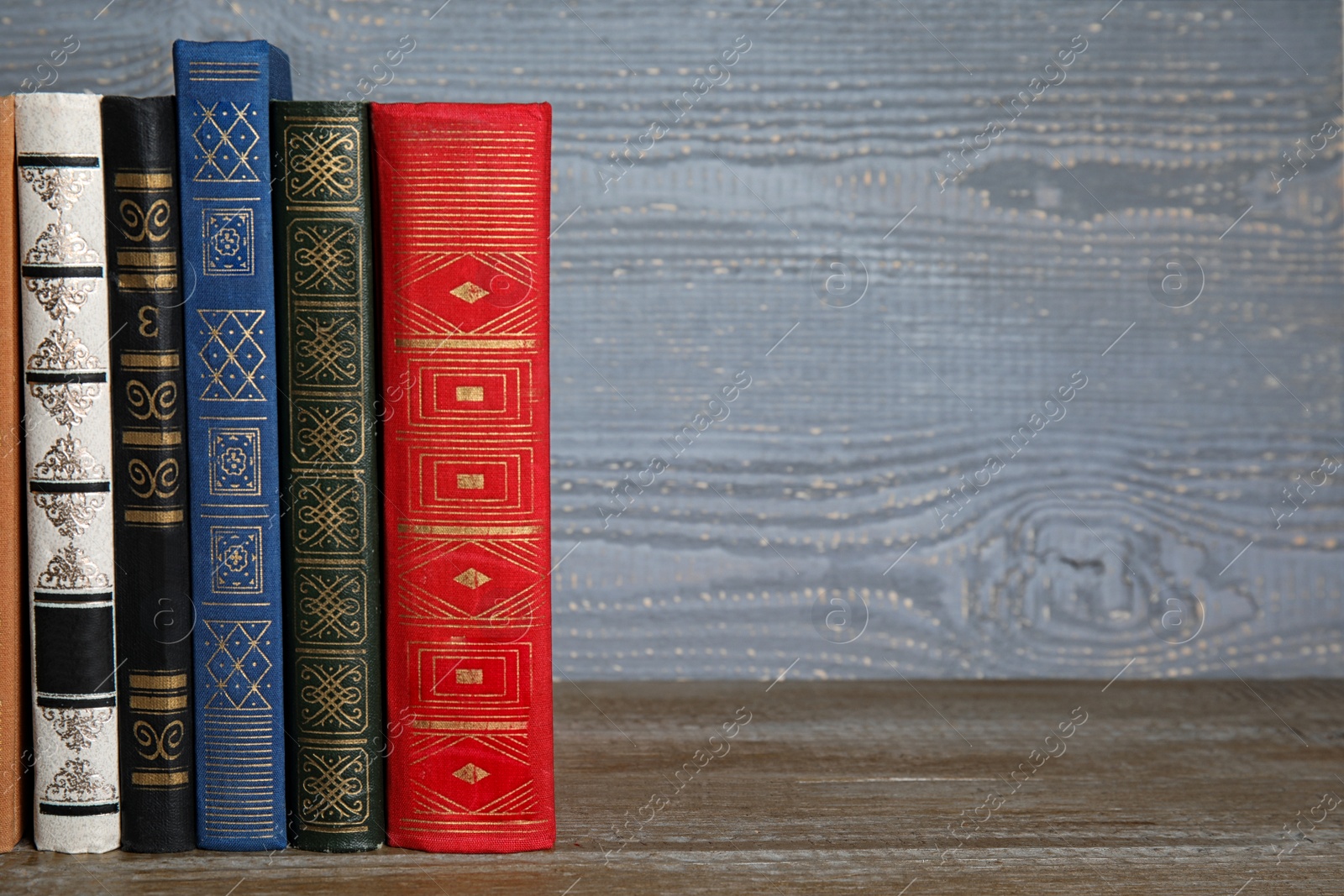 Photo of Stack of hardcover books on wooden table against grey background. Space for text