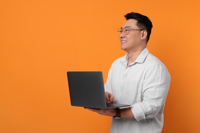 Photo of Happy man with laptop on orange background, space for text