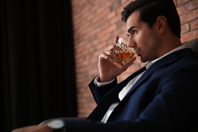 Photo of Young man with glass of whiskey near brick wall indoors. Space for text