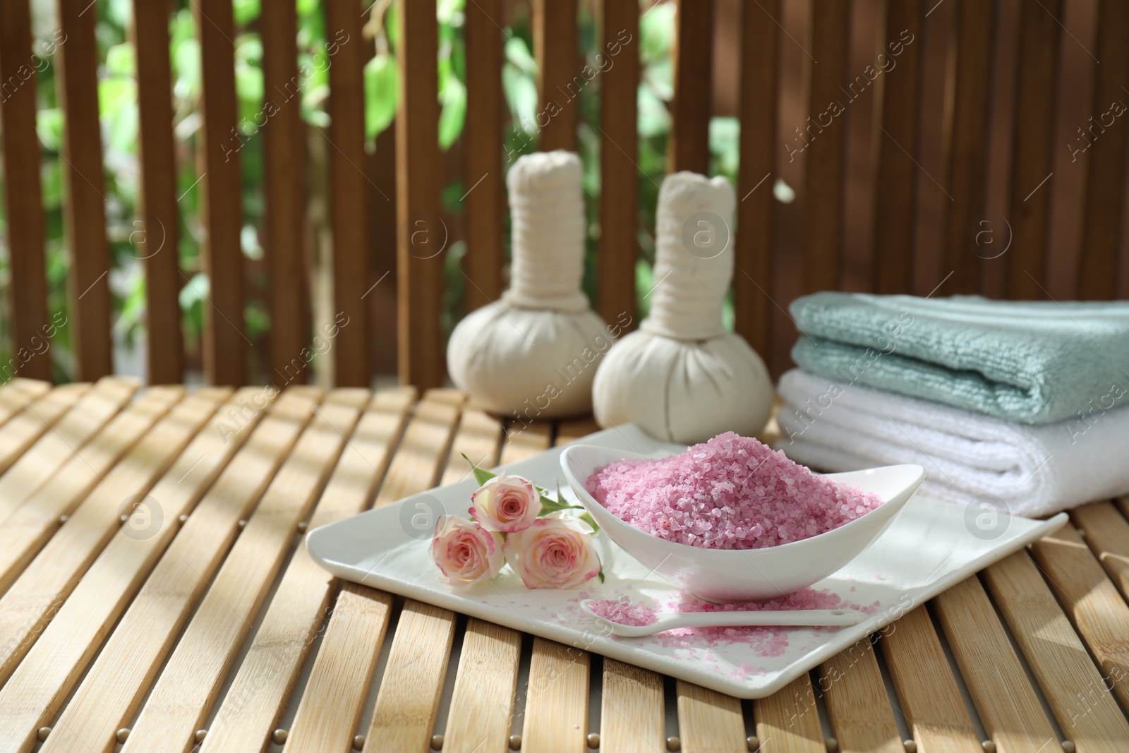 Photo of Bowl of pink sea salt and beautiful roses on wooden table, space for text