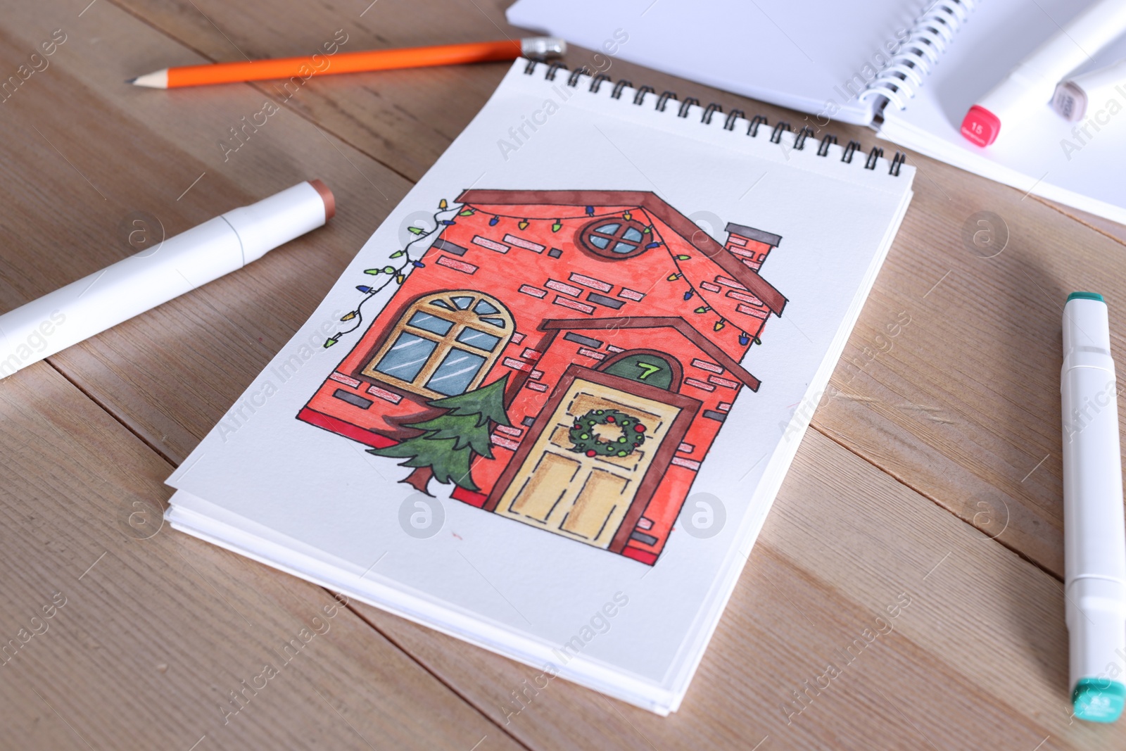 Photo of Sketchbook with beautiful drawing of house and felt tip pens on wooden table