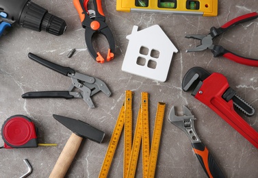 Photo of Flat lay composition with house figure and repair tools on grey marble table