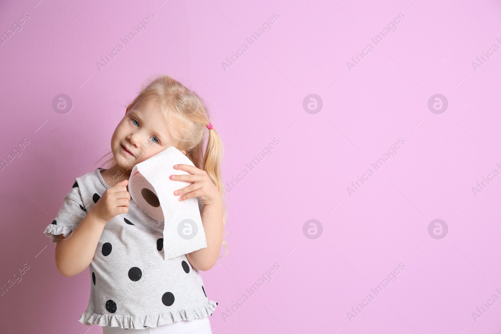 Photo of Cute little girl holding toilet paper roll on color background. Space for text