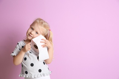 Photo of Cute little girl holding toilet paper roll on color background. Space for text