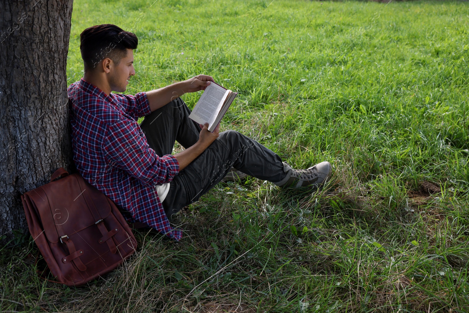 Photo of Handsome man reading book under tree on green meadow
