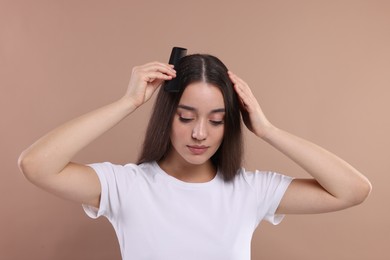 Photo of Woman with comb examining her hair and scalp on beige background. Dandruff problem