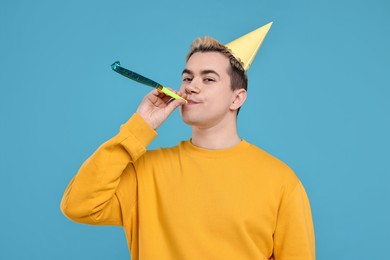 Young man with party hat and blower on light blue background