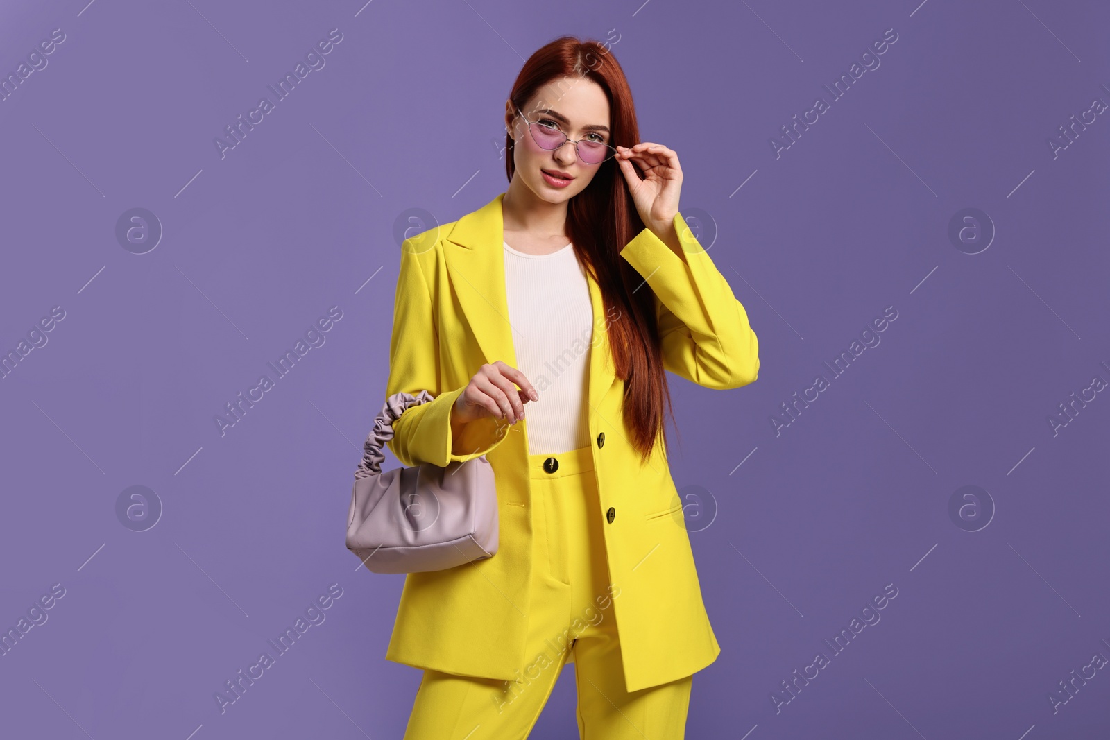 Photo of Stylish woman with red dyed hair and bag on purple background