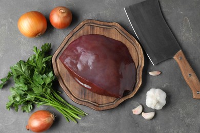 Piece of raw beef liver, knife and products on grey table, flat lay