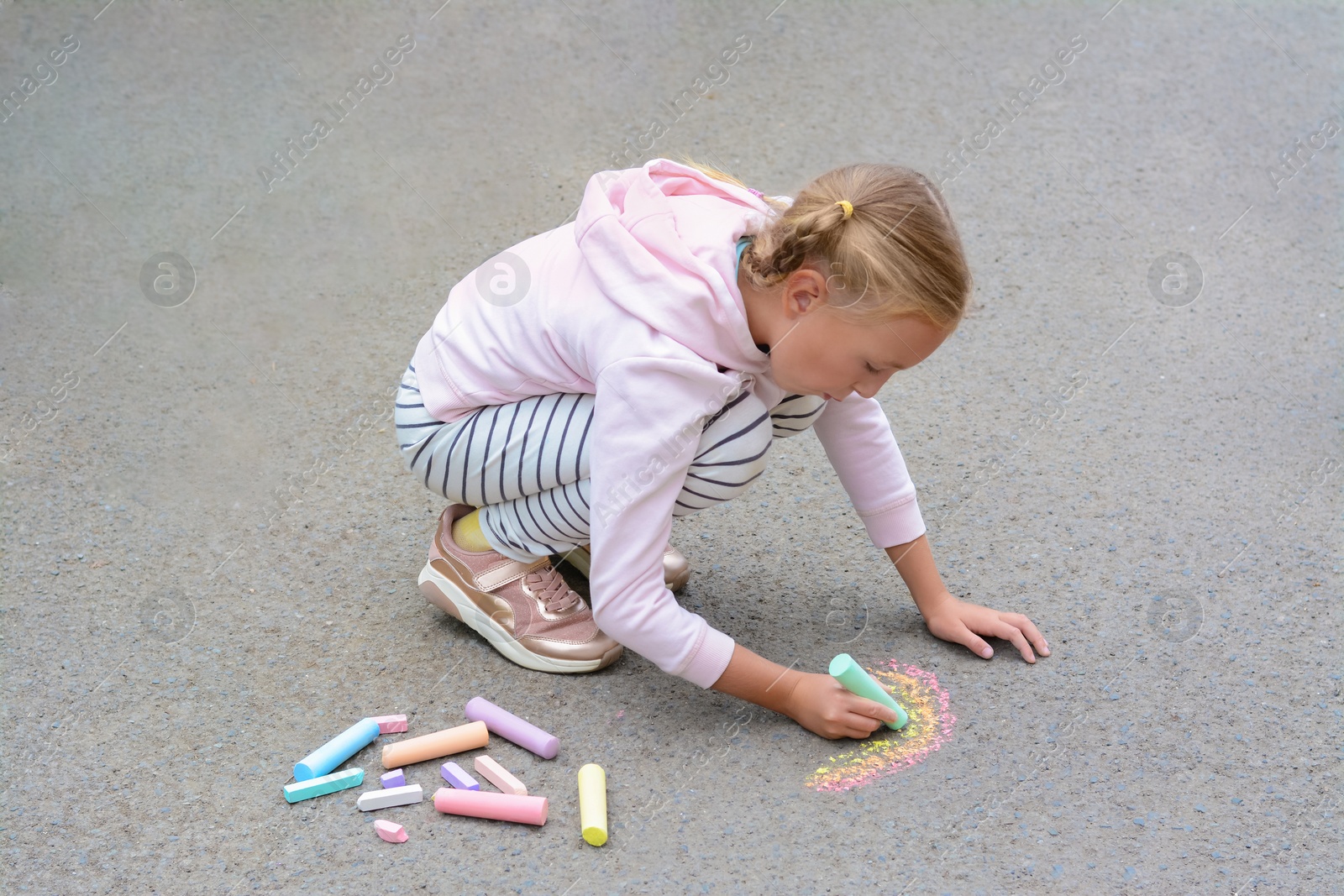 Photo of Little child drawing rainbow with chalk on asphalt