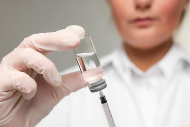 Photo of Doctor filling syringe with medication from glass vial on grey background, closeup