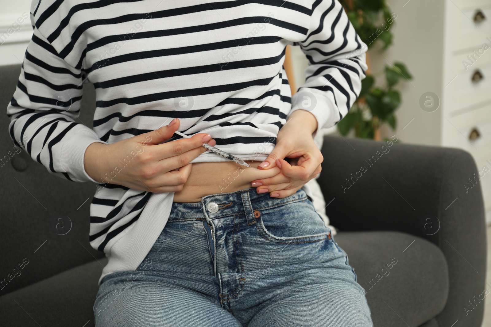 Photo of Diabetes. Woman making insulin injection into her belly on sofa indoors, closeup