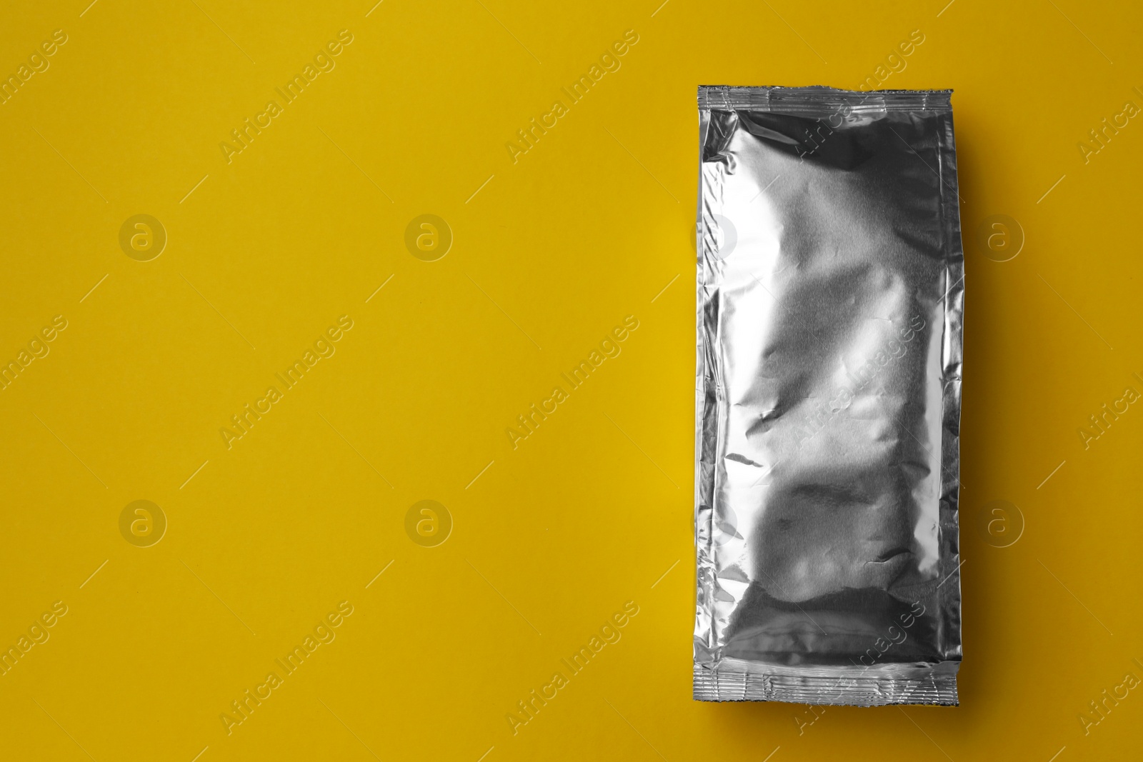 Photo of Blank foil package on yellow background, top view. Space for text