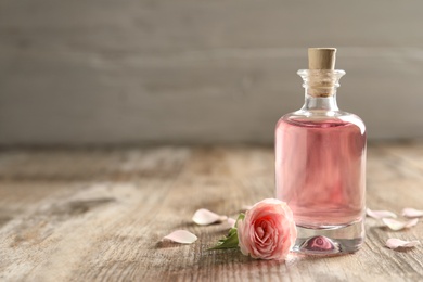 Photo of Bottle of rose essential oil and flower on wooden table, space for text