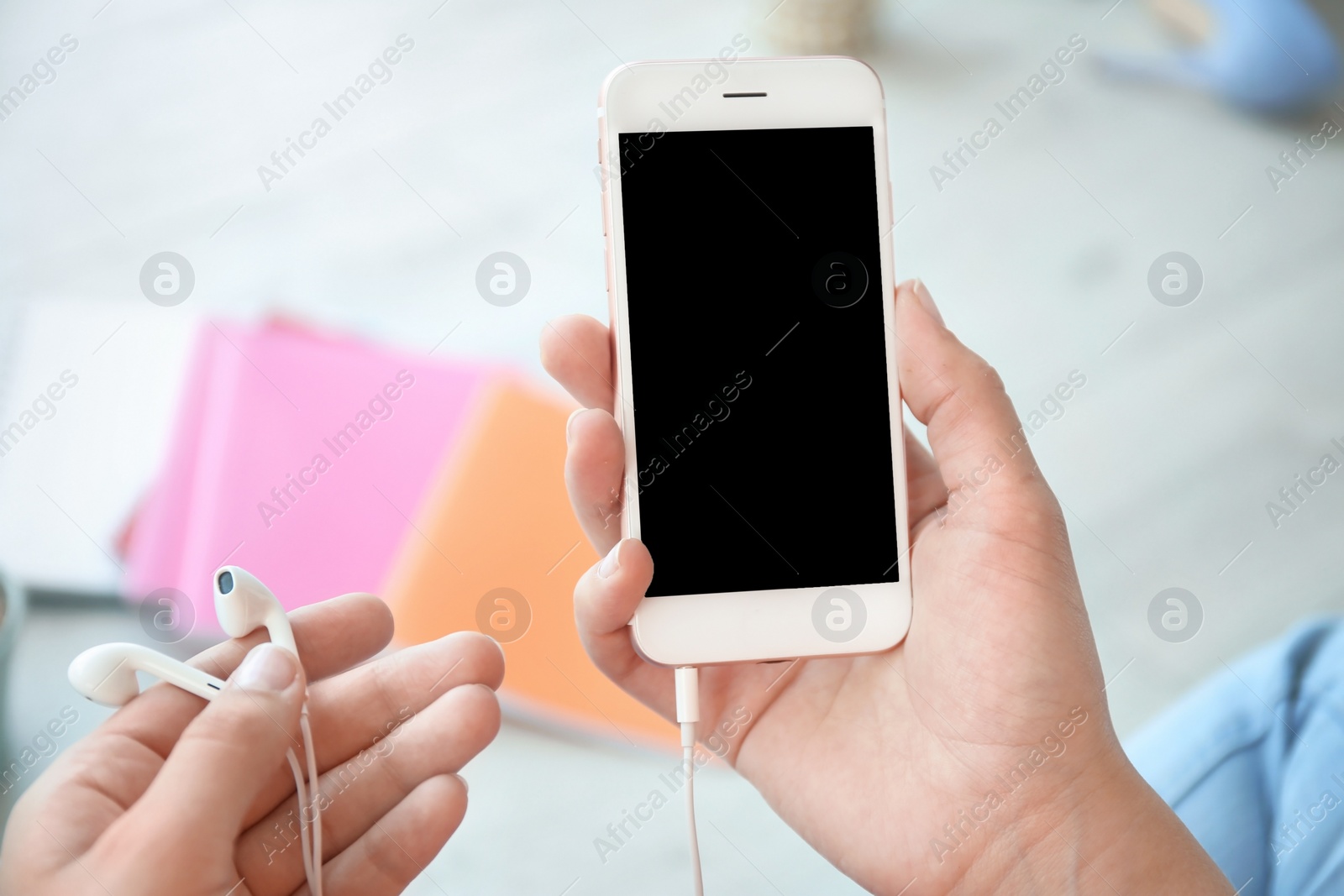 Photo of Young woman holding mobile phone with blank screen and earphones in hands, indoors