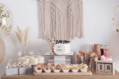 Baby shower party. Different delicious treats on wooden table and decor near light wall
