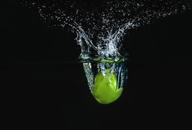 Photo of Ripe green apple falling down into clear water with splashes against black background
