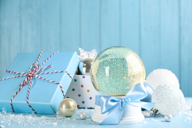 Photo of Beautiful snow globe, gift box and Christmas decor on light blue table