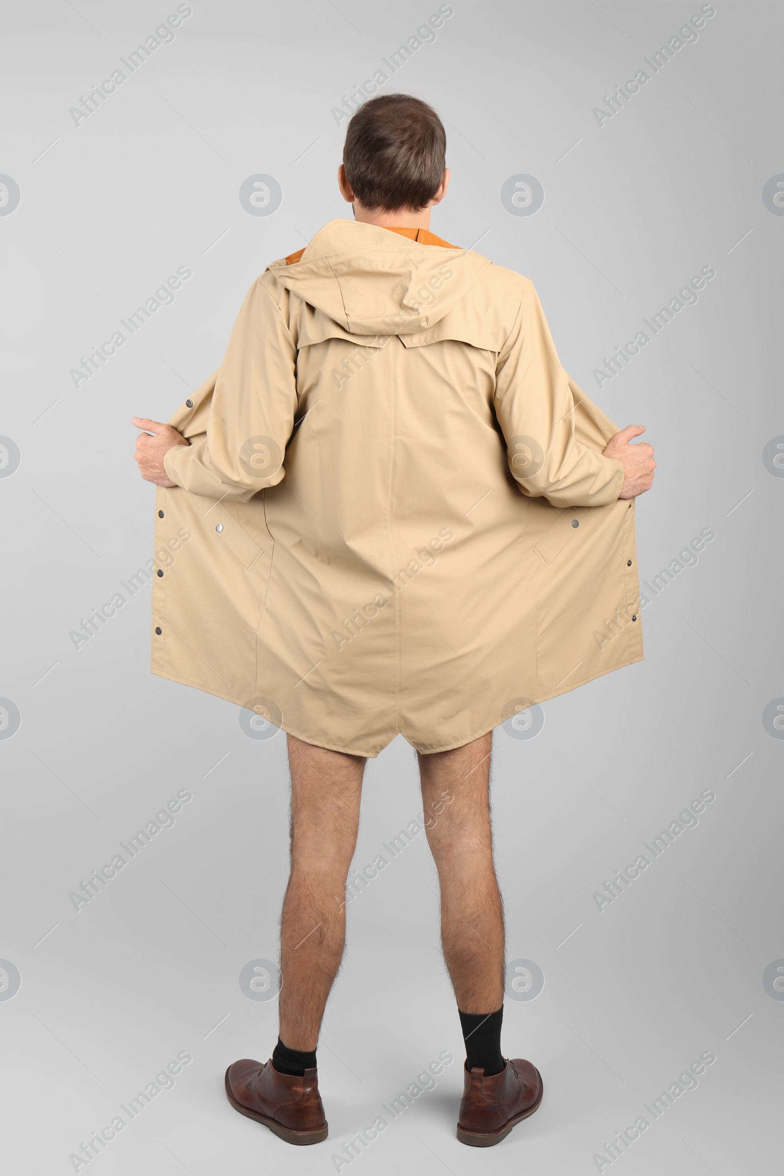 Photo of Exhibitionist exposing naked body under coat on light background, back view