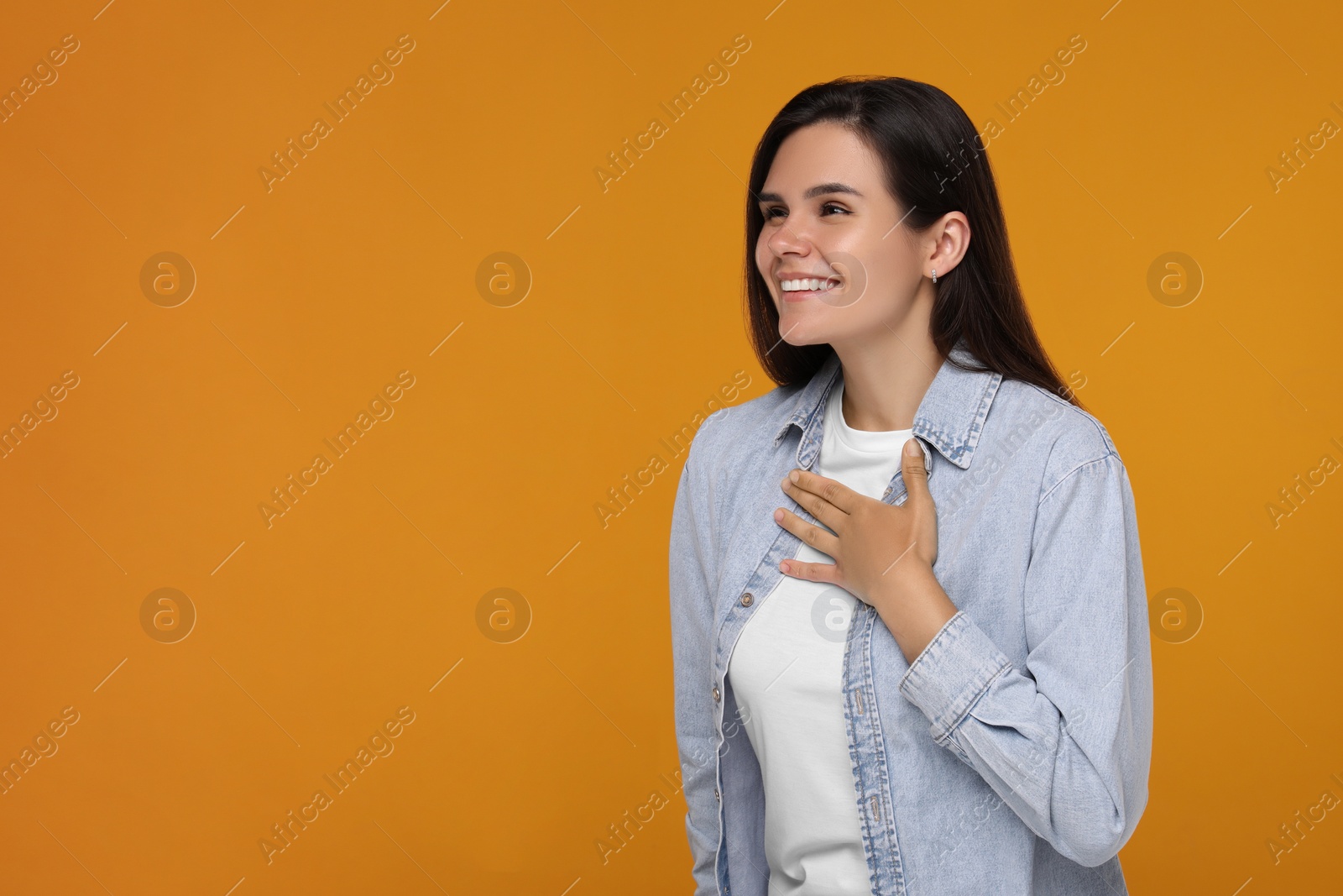 Photo of Thank you gesture. Happy grateful woman with hand on chest against orange background, space for text