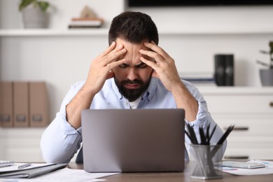 Photo of Man suffering from headache at workplace in office