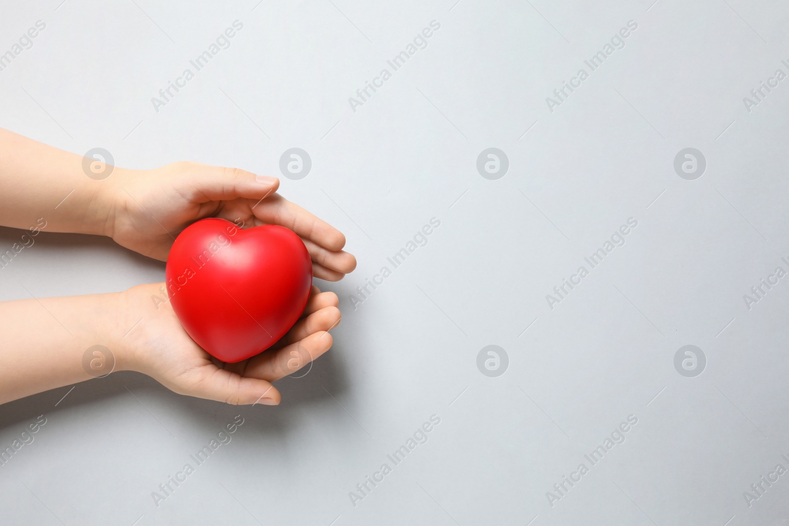 Photo of Child holding red heart on light grey background, top view. Space for text