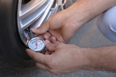 Photo of Man checking air pressure in car tire outdoors, closeup