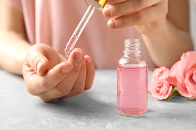 Photo of Woman dripping rose essential oil and bottle on finger at table, closeup