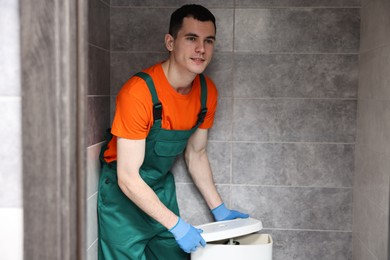 Photo of Young plumber repairing toilet bowl in water closet