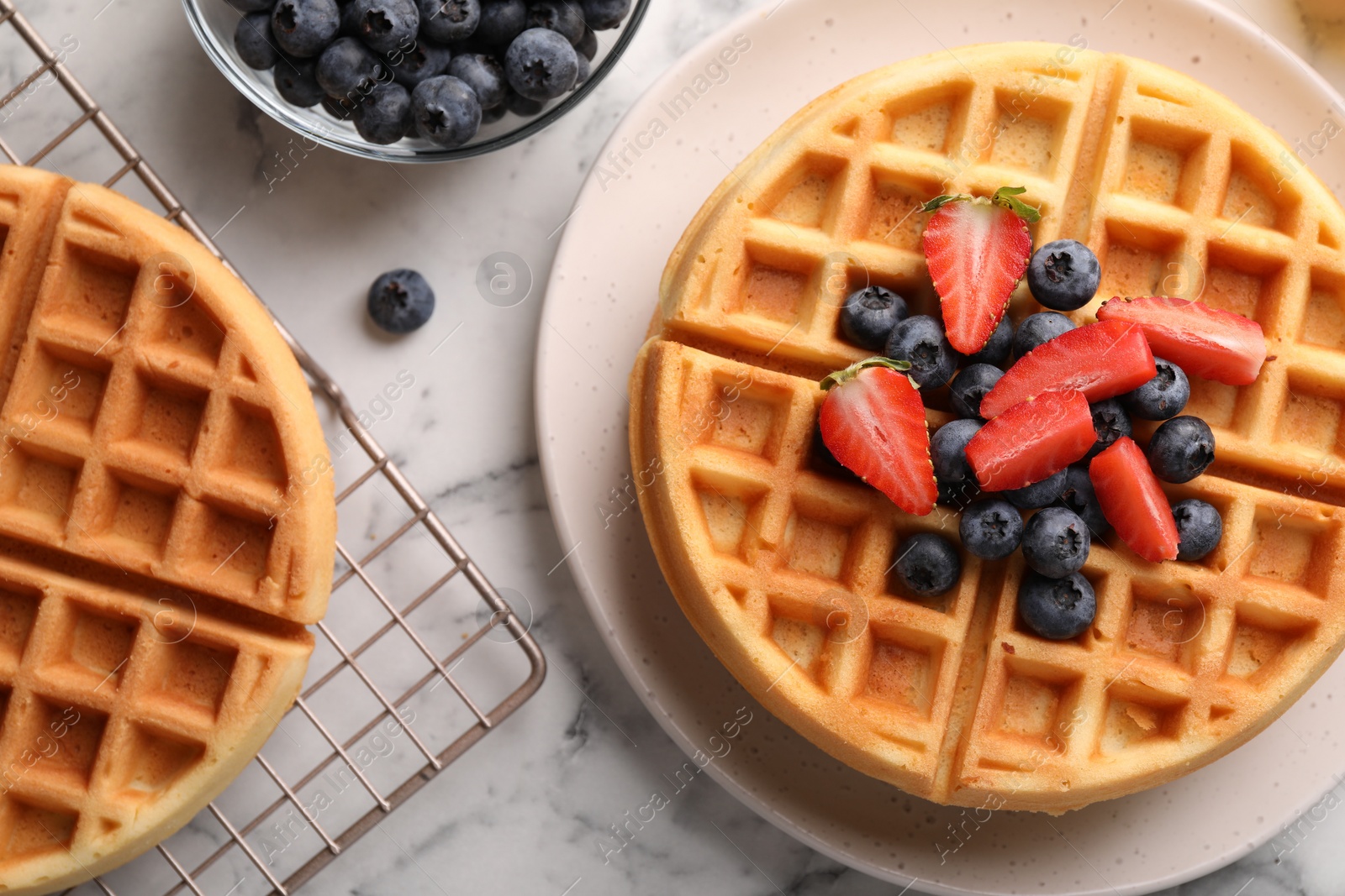 Photo of Tasty Belgian waffles with fresh berries on white marble table, flat lay