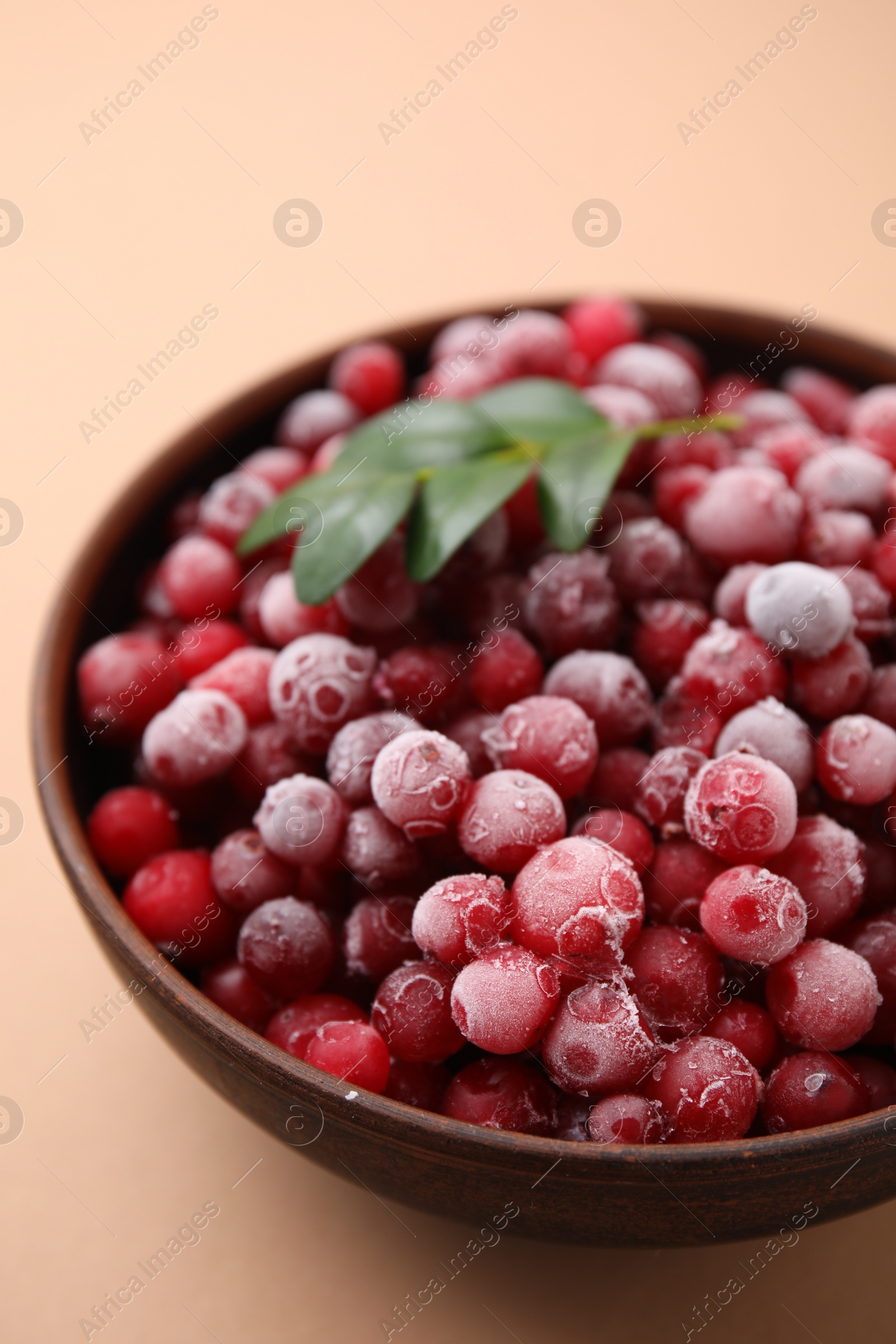 Photo of Frozen red cranberries and green leaves on beige background, closeup