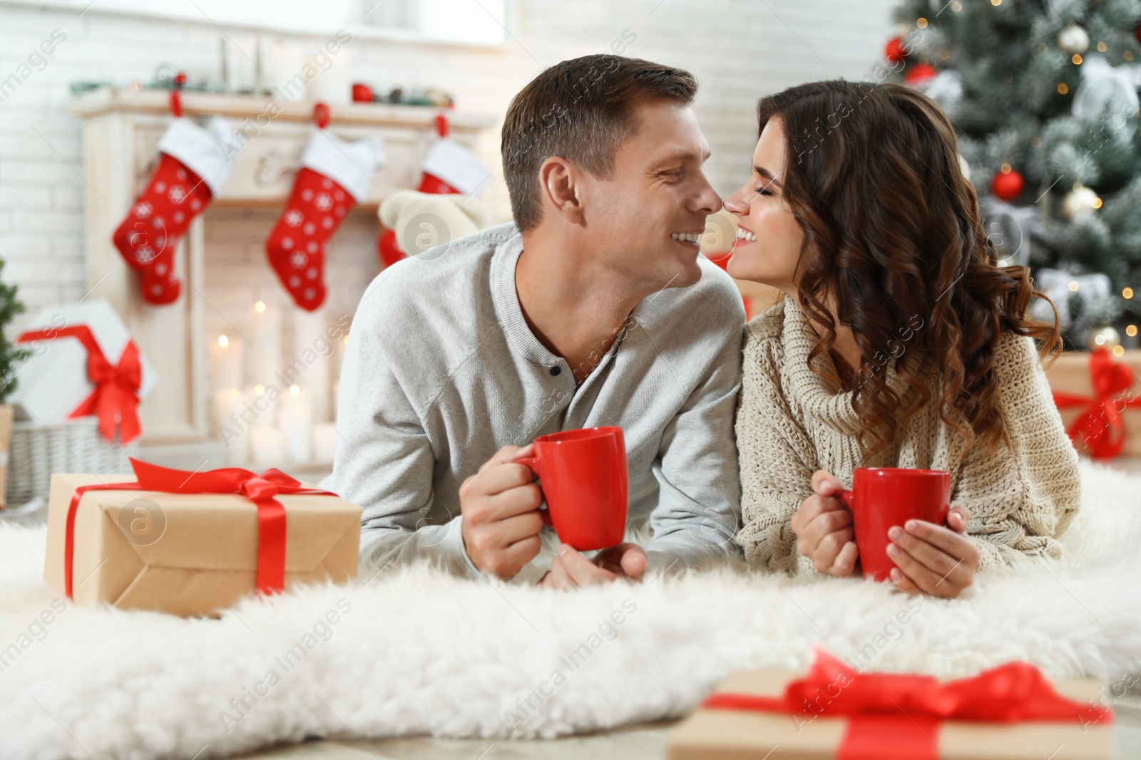 Image of Happy couple with cups of hot drink on floor in room decorated for Christmas