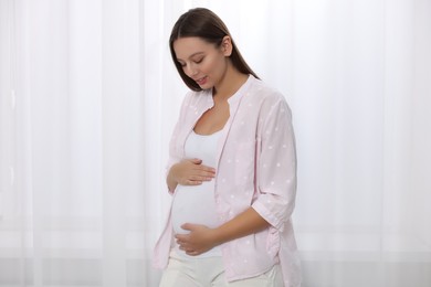 Photo of Beautiful pregnant woman in pink shirt near window indoors