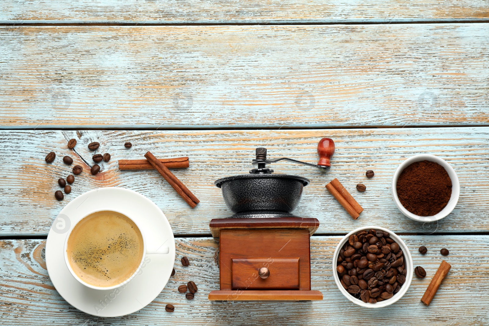 Photo of Vintage manual coffee grinder, cup of drink, cinnamon, powder and beans on wooden table, flat lay. Space for text