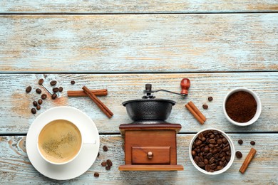 Vintage manual coffee grinder, cup of drink, cinnamon, powder and beans on wooden table, flat lay. Space for text