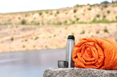 Photo of Sleeping bag and thermos outdoors on sunny day. Space for text
