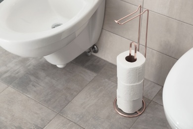 Photo of Holder with toilet paper rolls on floor in bathroom