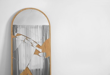 Photo of Broken mirror with many cracks near white wall. Space for text