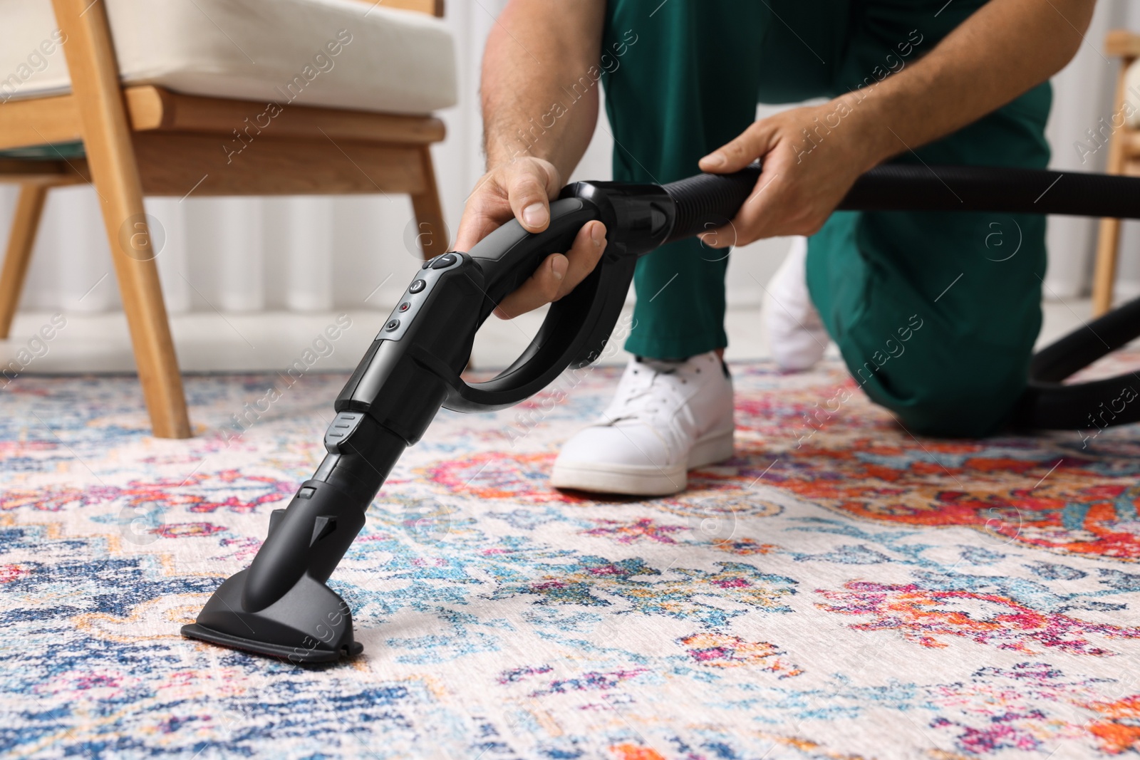 Photo of Dry cleaner's employee hoovering carpet with vacuum cleaner indoors, closeup